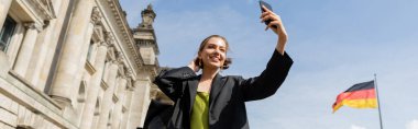 Gülümseyen kadın Berlin 'deki Reichstag binasının yakınında selfie çekiyor, afiş.