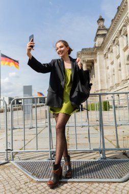 Sırt çantalı neşeli kadın Almanya, Berlin 'deki Reichstag Binası yakınlarında selfie çekiyor. 