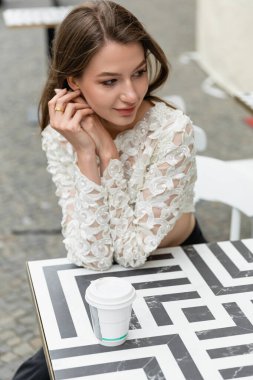 Süslü dantelli tişörtlü neşeli genç kadının portresi kahvenin yanında dinlenirken uzaklara bakıyor.