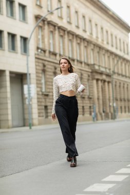 Almanya, Berlin 'de sokağa çıkmak için dantelli üst ve yüksek bel pantolonlu genç bir kadın elinde kahve tutuyor. 
