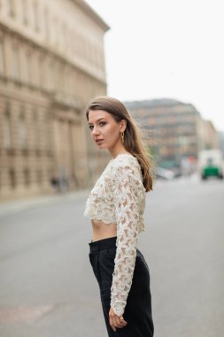 Almanya, Berlin 'de sokakta duran dantelli üst ve yüksek bel pantolonlu genç bir kadın. 