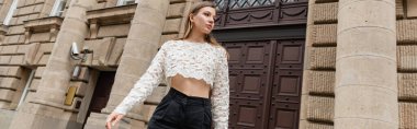 young woman in lace top and high waist pants looking away on urban street in Berlin, banner clipart
