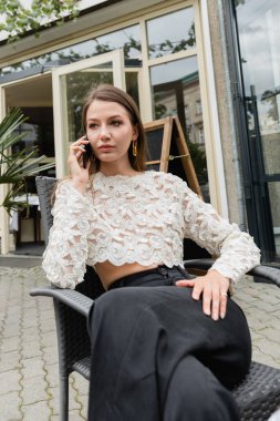 Berlin 'de caddenin terasında dinlenirken akıllı telefondan konuşan şık bir kadın.