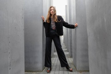 stylish young woman in jacket standing between Memorial to Murdered Jews of Europe in Berlin clipart