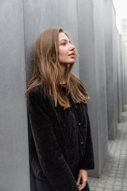 fair haired relaxed  woman in jacket standing between Memorial to Murdered Jews of Europe in Berlin clipart