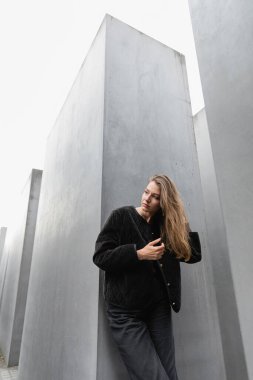 fair haired woman touching hair and looking away near Memorial to Murdered Jews of Europe in Berlin clipart