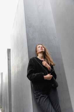 young fair haired woman in jacket standing between Memorial to Murdered Jews of Europe in Berlin clipart
