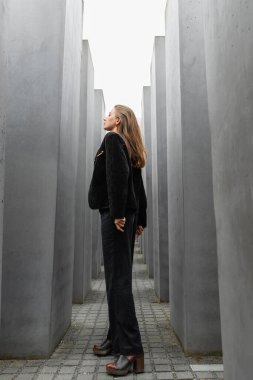 woman in black jacket looking away while standing between Memorial to Murdered Jews of Europe  clipart