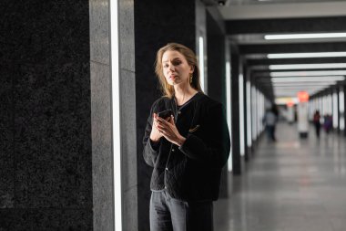 Berlin 'de florasan lambalarla modern binada poz veren siyah ceketli güzel ve genç bir kadın.