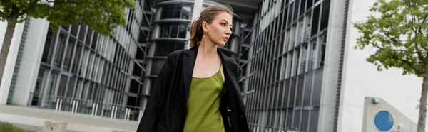 stock image young fair haired woman in green silk dress and blazer walking in Berlin, Germany, banner 