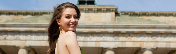 Smiling woman looking at camera while standing near Brandenburg Gate in Berlin, Germany, banner 
