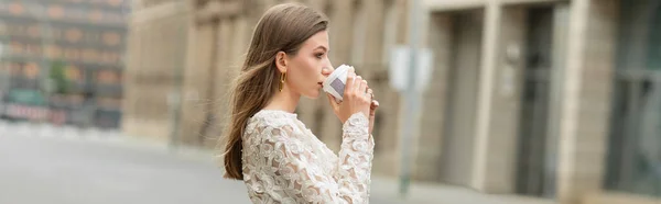 stock image Side view of trendy young fair haired woman in white lace top drinking coffee to go, banner 