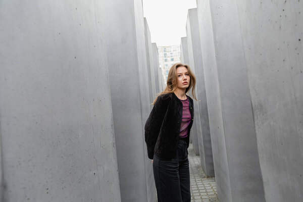 fair haired young woman in jacket standing between Memorial to Murdered Jews of Europe in Berlin
