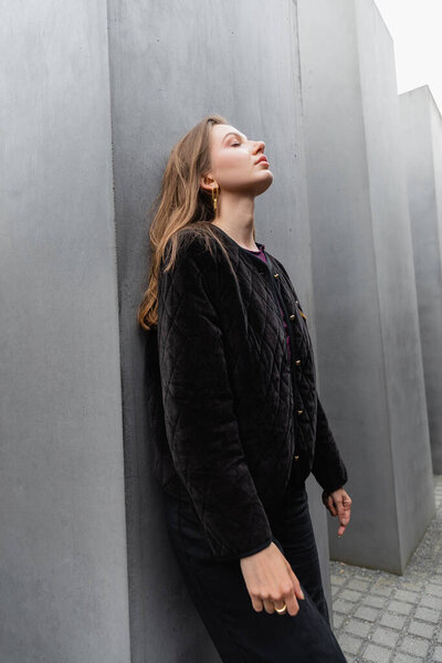 Relaxed young woman in jacket standing near Memorial to Murdered Jews of Europe at daytime in Berlin