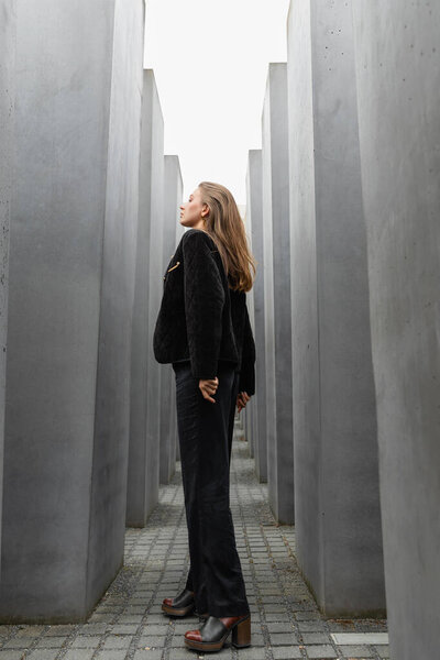 woman in black jacket looking away while standing between Memorial to Murdered Jews of Europe 