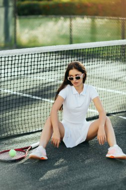 active lifestyle, tennis court in Miami, athletic young woman with brunette long hair sitting in white outfit and sunglasses near racket and ball, tennis net, blurred background, iconic city  clipart
