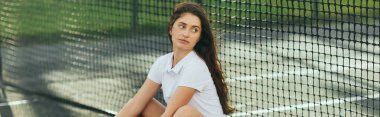 Tenis ağının yanında oturan bayan oyuncu, uzun saçlı, beyaz polo tişörtlü, tenis kortuna bakan genç kadın, bulanık arka plan, Miami, ikonik şehir, fiziksel aktivite, afiş