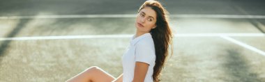 Kadın tenisçi maçtan sonra dinleniyor, beyaz elbisesiyle asfaltta oturuyor ve kafasını çeviriyor, geçmişi bulanık, Miami, tenis kortu, dinlenme zamanı, polo tişörtü, pankart 