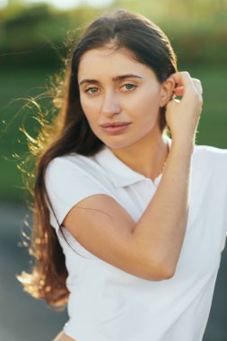 Esmer, uzun saçlı çekici bir kadının portresi beyaz polo gömlekli ve kameraya bakıyor bulanık arka plan, Miami, Florida, ikonik şehir, doğal makyaj.