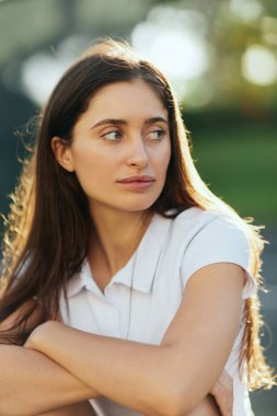portrait of young woman with brunette long hair posing in white polo shirt and looking away, blurred background, Miami, Florida, iconic city, natural makeup, minimalistic  clipart