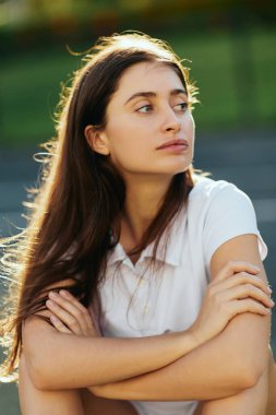 portrait of young woman with brunette long hair and natural makeup posing with crossed arms in white polo shirt and looking away, blurred background, Miami, Florida, iconic city,  clipart