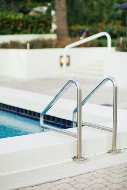 Açık havuz, parlak mavi su ve metalik havuz merdiveni lüks otel otelinde paslanmaz tırabzanlar, bulanık arka plan, tatil ve tatil konsepti. 