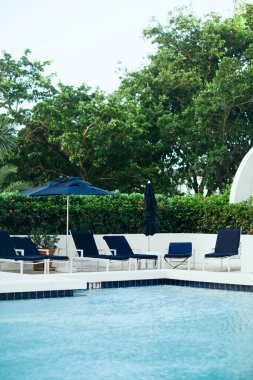 Lüks tatil beldesi, tatil ve tatil konsepti, güneşli yataklar ve şemsiyelerin yanındaki açık sandalyeler yeşil tropikal palmiye ağaçları ve oteldeki açık havuzun yanındaki bitkiler, yaz mevsimi.