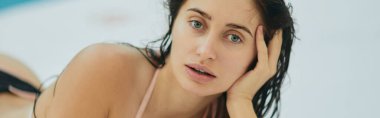 Bikinili esmer kadın, ıslak saçlı, lüks bir tatil köyünde poz veren seksi manken, Miami, Florida, ABD, bulanık arka plan, beyaz yüzeye uzanmış, havuz kenarında rahatlama, kameraya bakma, afiş. 