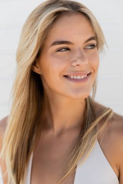A young blonde woman with long hair smiles warmly at the camera on a sunny day at Miami Beach. clipart