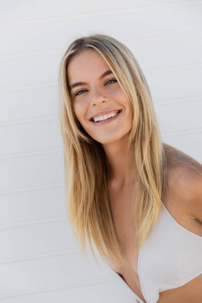 A young blonde woman in a white top smiles brightly against the backdrop of Miami Beach.