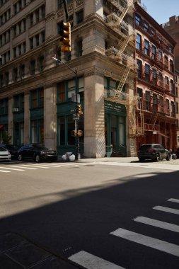 corner building with fire escape stairs and cars on crossroad on downtown street of new york city clipart