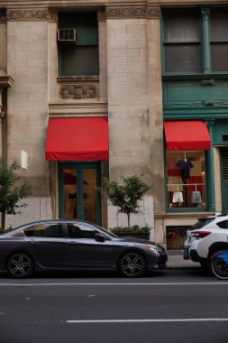 New York 'un merkezinde giysi mağazası ve kırmızı tenteleri olan klasik binanın yakınına park edilmiş arabalar.