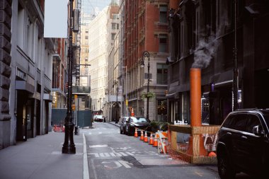 New York 'un dar sokaklarında park etmiş arabaların yanında buharlı havalandırma borusu, metropol atmosferi.