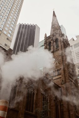 Gökdelenlerin yakınındaki kırmızı tuğlalı katolik kilisenin alçak açılı görüntüsü ve New York caddesinde buhar.