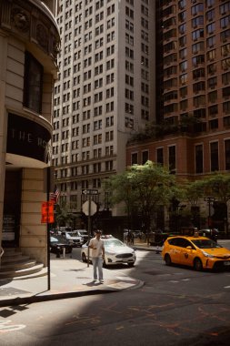 NEW YORK, USA - NOVEMBER 26, 2022: man walking on sidewalk near crossroad with moving cars clipart