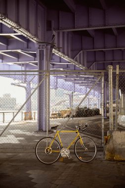 yellow bicycle near metallic net fence over bridge in new york city, contemporary metropolis scene clipart