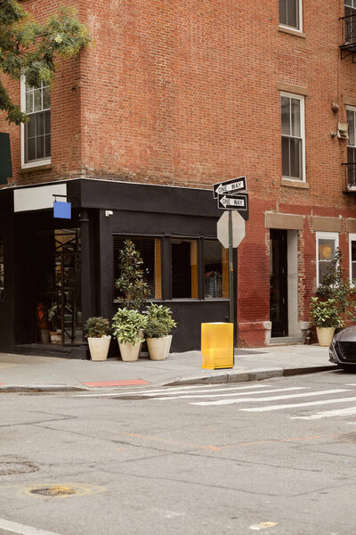 brick building with storefront and flowerpots near crossroad on urban street in new york city