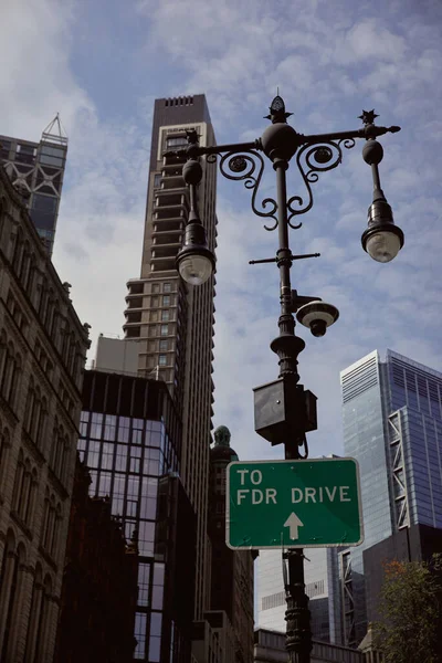 street pole with lanterns and traffic sign against modern building and skyscrapers in new york city
