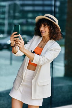 Beyaz ceketli ve etekli bir kadın bir Avrupa şehrinde selfie için poz veriyor..