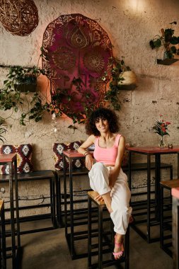 A woman in stylish clothing sits in a European cafe, enjoying the atmosphere. clipart