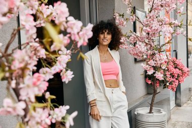 Bir Avrupa şehrinde çiçek açan bir ağacın yanında şık bir kadın duruyor..