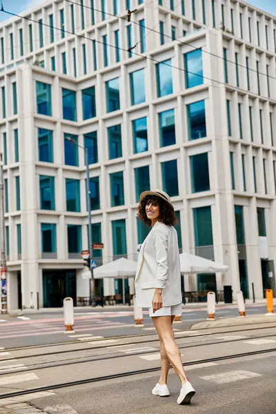 stock image A woman in a white outfit walks across a street in a European city.