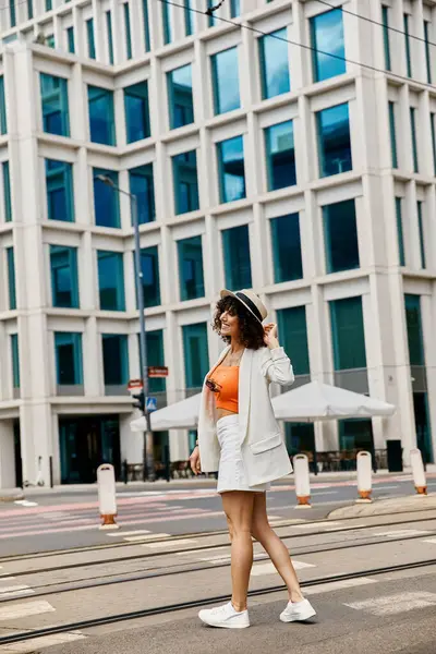 stock image A woman in a white blazer and skirt walks across a city street, showcasing a stylish outfit.