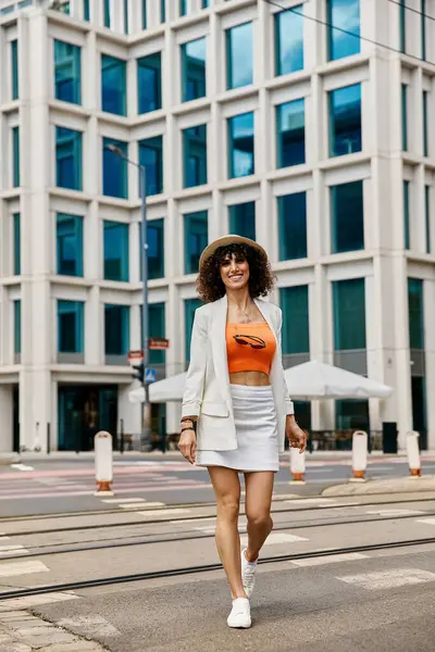 stock image A woman in a white blazer and skirt walks down a city street in Europe.