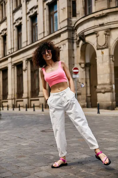 stock image A woman in a pink crop top and white pants strolls through the streets of Europe.