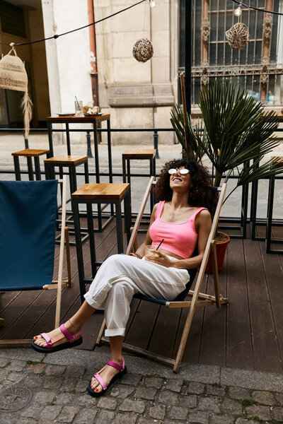 A stylish woman relaxes in a cafe chair, enjoying the summer sun in a European city.
