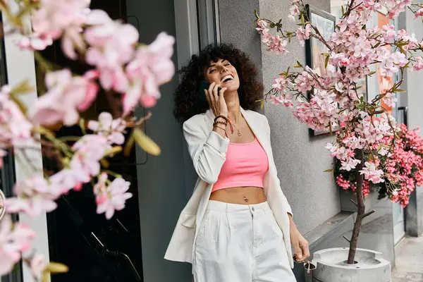 stock image A woman in a white blazer and pink top smiles while on a phone call in a European city.