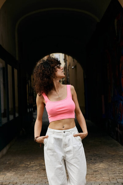 A woman in stylish attire walks through an archway in a European city.
