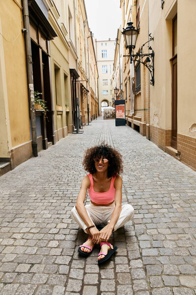 A beautiful woman sits on a cobblestone street in Europe, enjoying her trip.