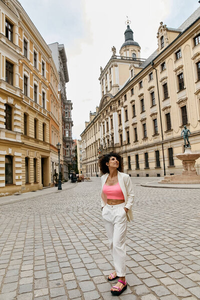 A woman in a white pantsuit strolls through a European city, enjoying the charming cobblestone streets.